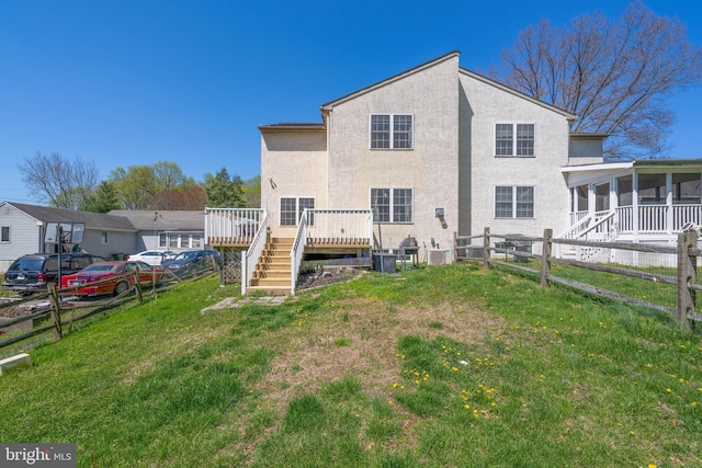 rear view of house featuring a lawn, a deck, fence, stucco siding, and a sunroom