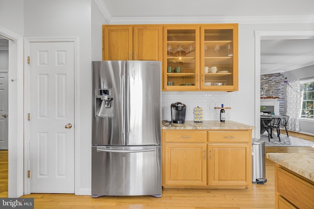 kitchen with light wood-style floors, stainless steel fridge with ice dispenser, backsplash, ornamental molding, and light stone countertops
