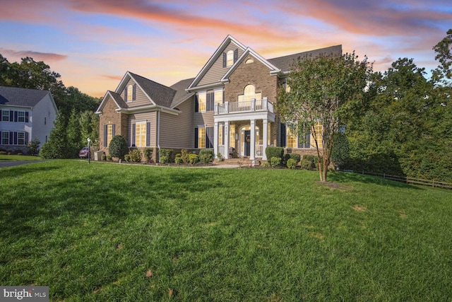 georgian-style home featuring a balcony, a lawn, and brick siding