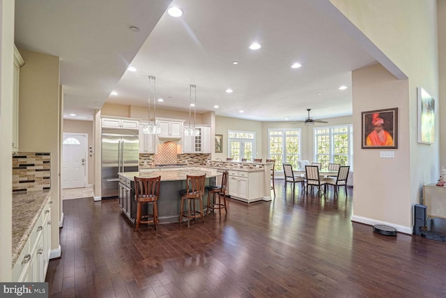kitchen featuring a breakfast bar area, a peninsula, stainless steel built in fridge, a center island, and dark wood-type flooring