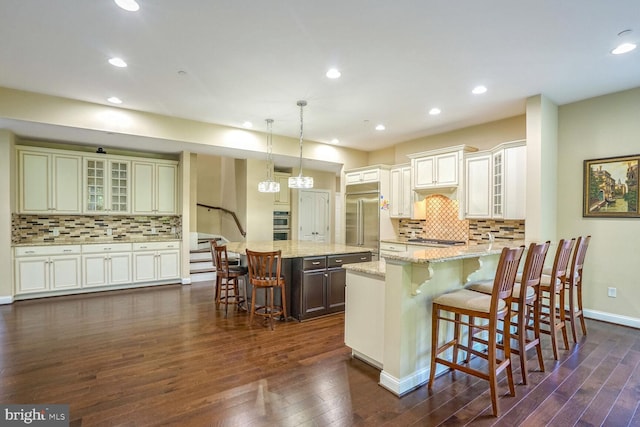 kitchen with tasteful backsplash, a kitchen bar, appliances with stainless steel finishes, glass insert cabinets, and dark wood-style flooring