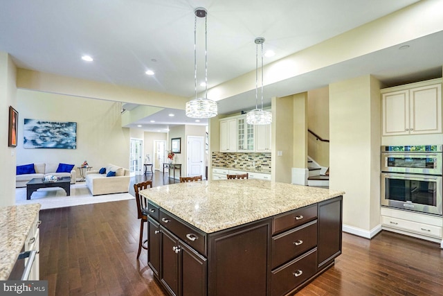 kitchen featuring double oven, light stone countertops, open floor plan, decorative backsplash, and dark wood-type flooring