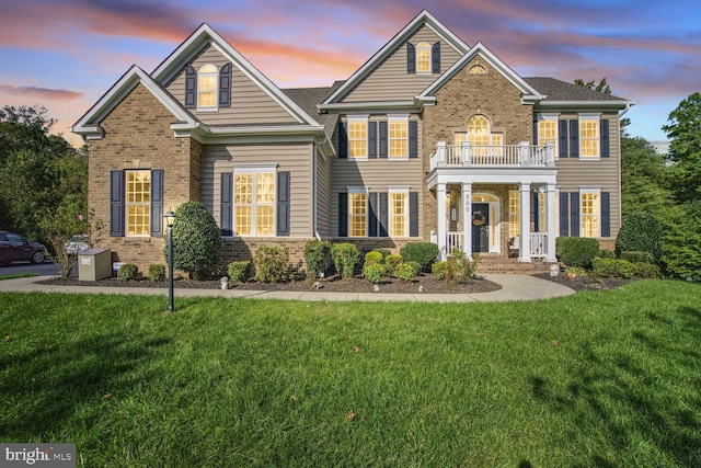 view of front of home with a balcony, brick siding, and a lawn