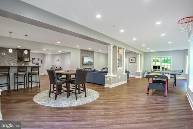 dining room featuring dark wood-style flooring, ornate columns, baseboards, recessed lighting, and bar