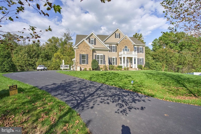 colonial home featuring brick siding, a front yard, driveway, and a balcony