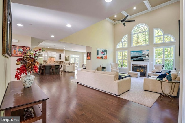 living room with a wealth of natural light, dark wood-type flooring, a glass covered fireplace, and ceiling fan