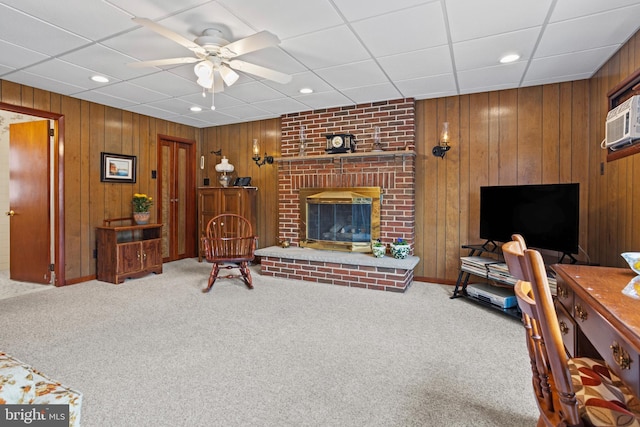 carpeted living room with a ceiling fan, wooden walls, recessed lighting, a fireplace, and a paneled ceiling
