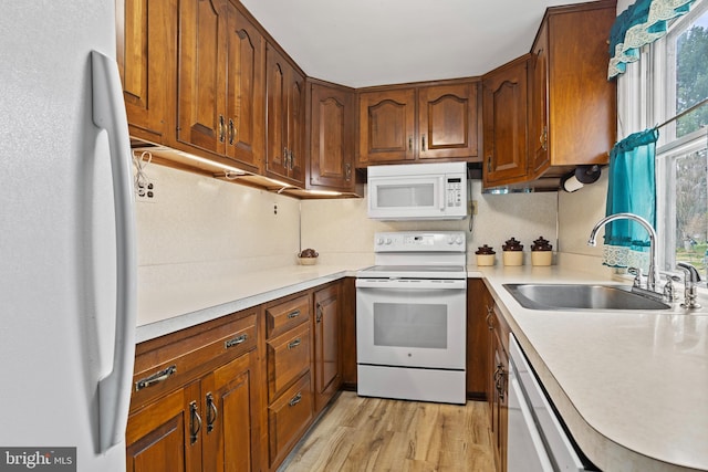 kitchen featuring white appliances, a sink, light countertops, light wood finished floors, and brown cabinetry