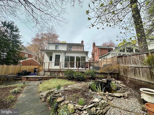 rear view of property featuring a deck, a chimney, a fenced backyard, and a patio area