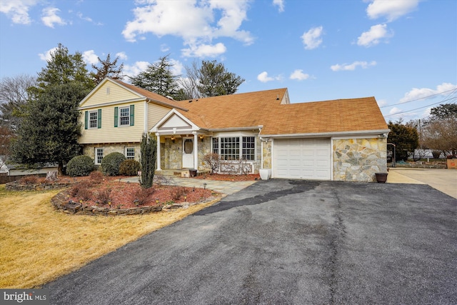 split level home featuring stone siding, driveway, a garage, and a front yard