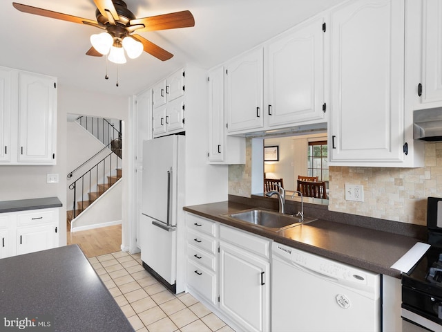 kitchen featuring white appliances, ceiling fan, dark countertops, under cabinet range hood, and a sink