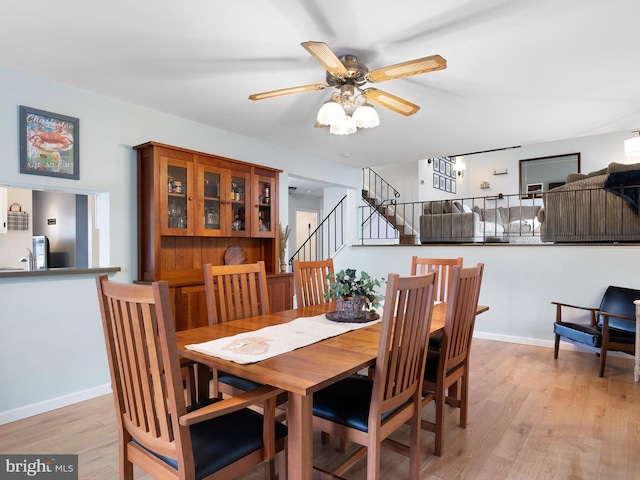 dining area with a ceiling fan, light wood-style flooring, baseboards, and stairs