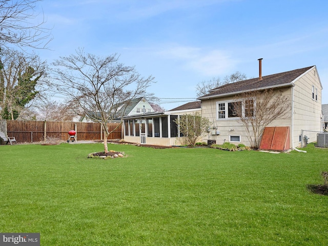 rear view of property with a fenced backyard, a sunroom, central AC unit, and a lawn
