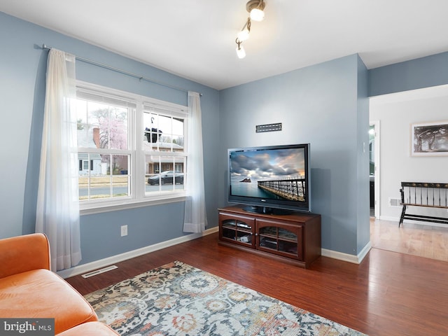 living area featuring baseboards, visible vents, and wood finished floors