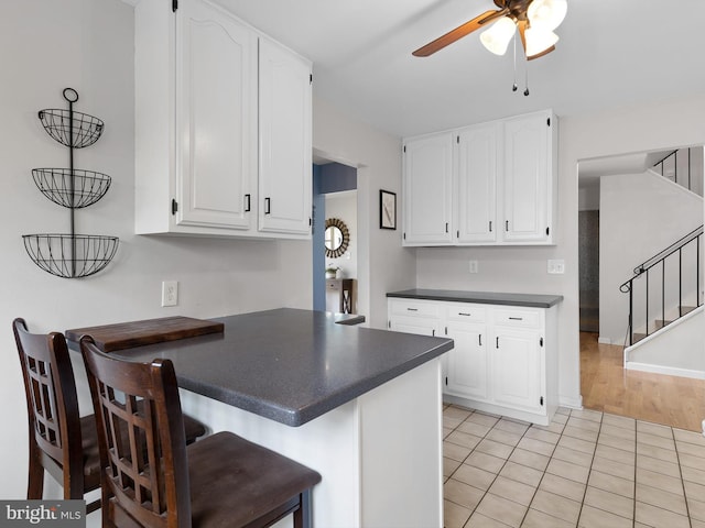 kitchen with white cabinets, a ceiling fan, a peninsula, and dark countertops