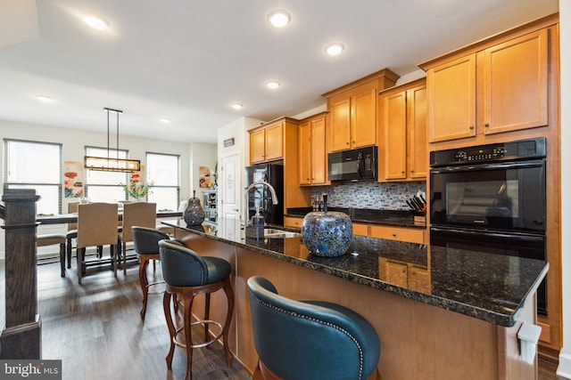 kitchen featuring tasteful backsplash, recessed lighting, a center island with sink, dark wood finished floors, and black appliances