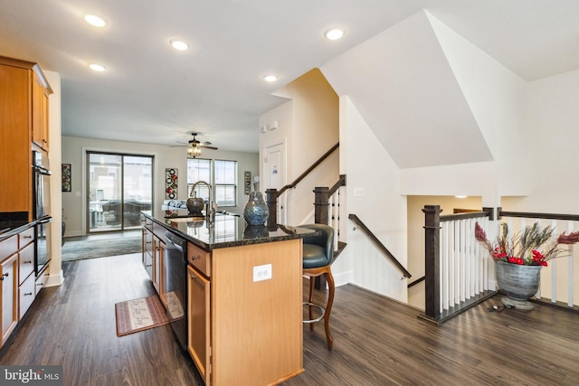 kitchen featuring dishwasher, a sink, a ceiling fan, dark wood-type flooring, and a breakfast bar area