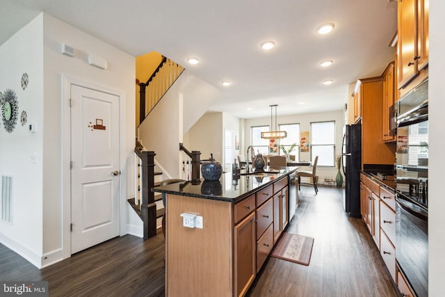 kitchen featuring baseboards, an island with sink, black appliances, dark wood-type flooring, and a sink