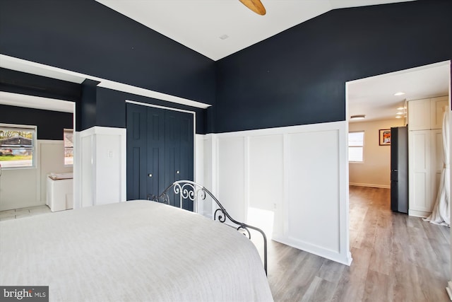 unfurnished bedroom with light wood-style flooring, wainscoting, and vaulted ceiling