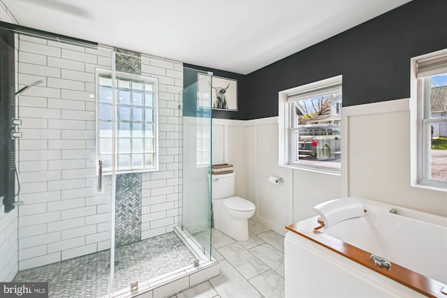 full bath featuring toilet, a stall shower, a bath, and a wainscoted wall