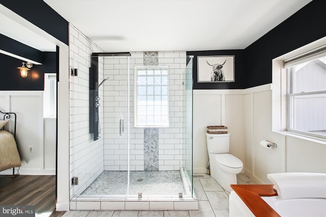 bathroom featuring a wealth of natural light, wainscoting, a shower stall, and toilet
