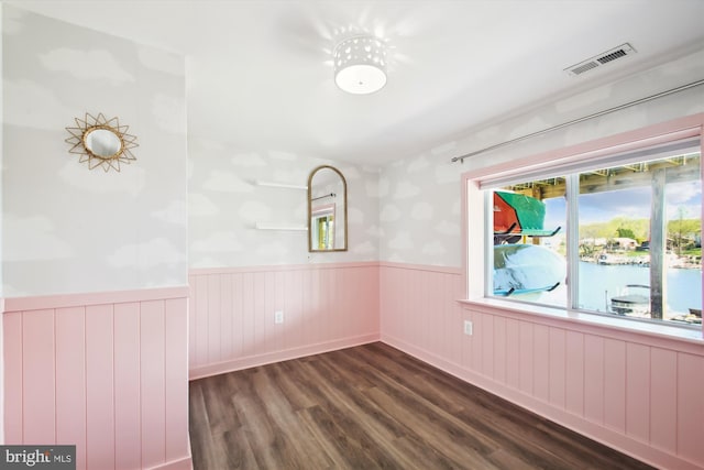 spare room featuring dark wood-style floors, visible vents, and wainscoting