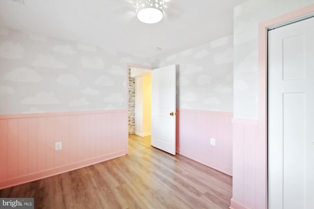 unfurnished bedroom featuring a closet, a wainscoted wall, and wood finished floors