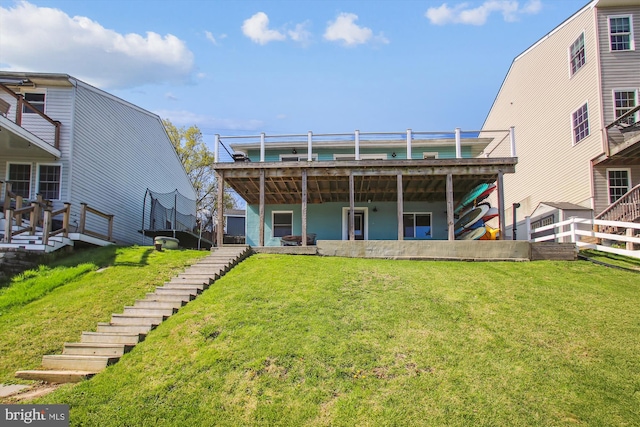 back of house with a trampoline, a yard, and stairway