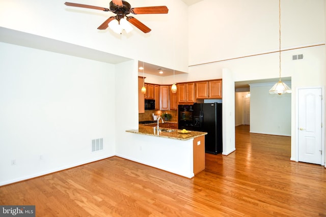 20559 Crescent Pointe Pl, Ashburn, VA 20147 - kitchen featuring black appliances, a peninsula, brown cabinets, light wood-style flooring, and a high ceiling
