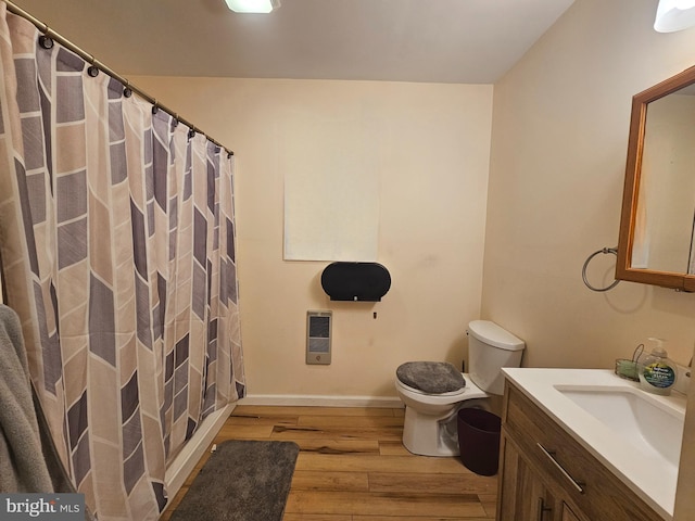 full bath featuring heating unit, toilet, vanity, wood finished floors, and baseboards