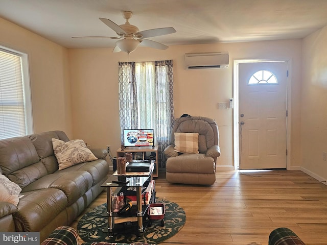 living area featuring baseboards, a wall mounted air conditioner, light wood finished floors, and ceiling fan