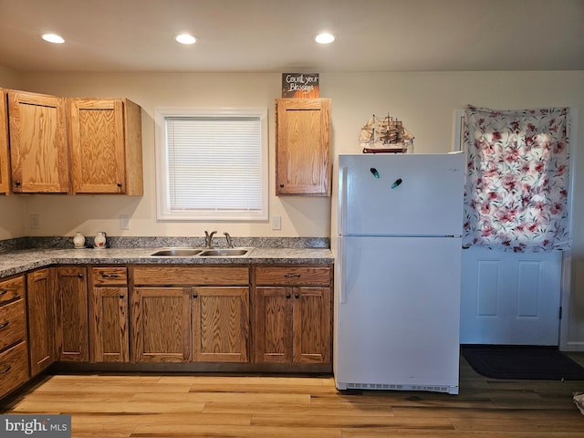 kitchen with freestanding refrigerator, a sink, dark countertops, and light wood-type flooring