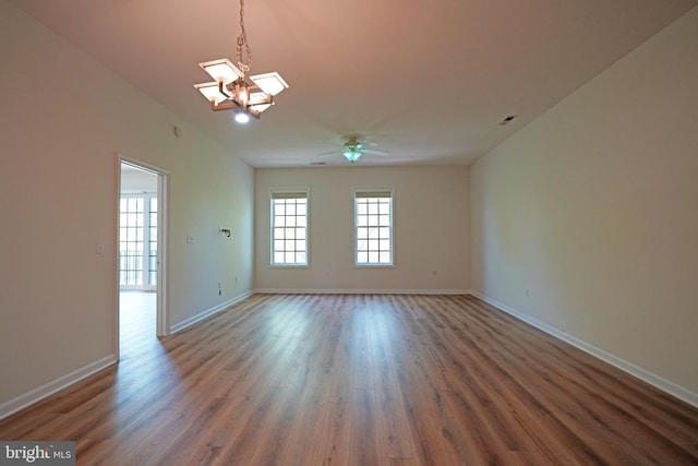empty room with a chandelier, wood finished floors, a ceiling fan, and baseboards