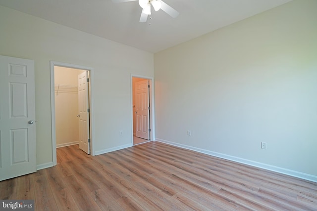 unfurnished bedroom featuring light wood-type flooring, a walk in closet, baseboards, a closet, and a ceiling fan
