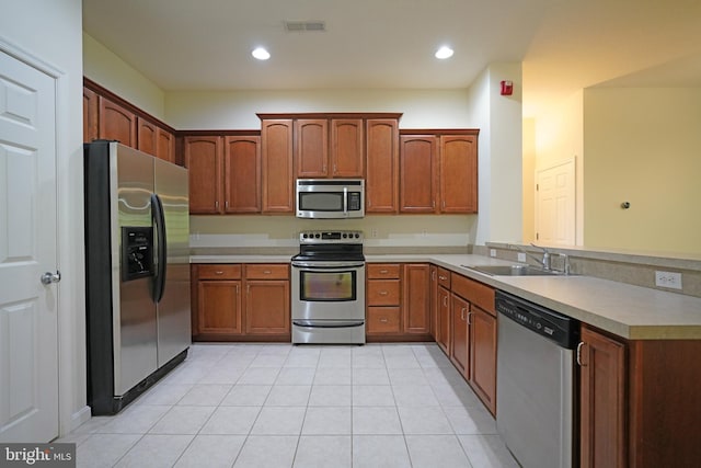 kitchen with appliances with stainless steel finishes, a sink, light countertops, a peninsula, and light tile patterned floors
