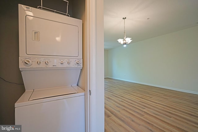 clothes washing area featuring stacked washer and clothes dryer, wood finished floors, baseboards, and a chandelier