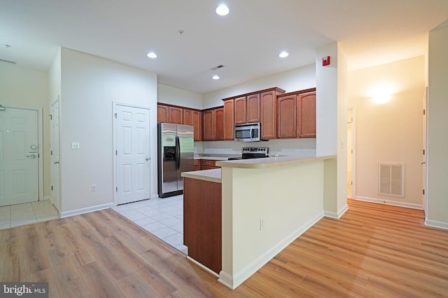 kitchen featuring appliances with stainless steel finishes, light wood-type flooring, light countertops, a peninsula, and recessed lighting