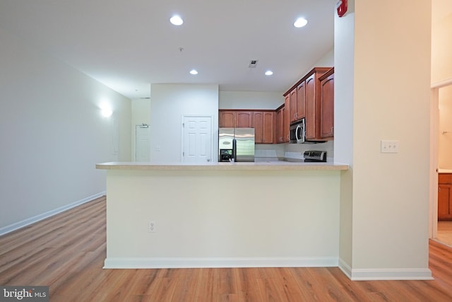 kitchen with appliances with stainless steel finishes, light wood-style floors, light countertops, a peninsula, and recessed lighting