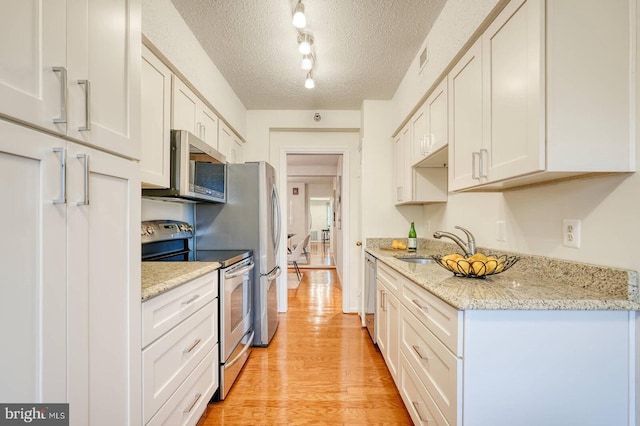 kitchen featuring rail lighting, light wood-style flooring, a textured ceiling, white cabinetry, and appliances with stainless steel finishes