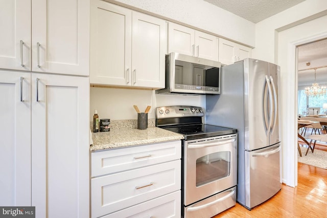 kitchen featuring appliances with stainless steel finishes, a chandelier, a textured ceiling, white cabinetry, and light wood finished floors