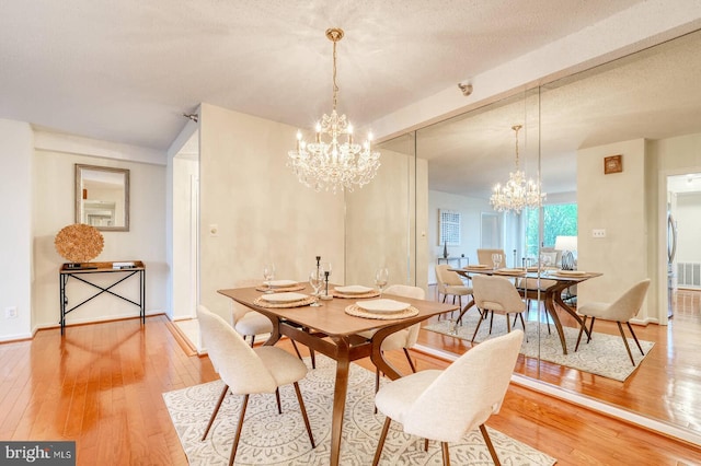 dining space with baseboards, visible vents, hardwood / wood-style flooring, and an inviting chandelier