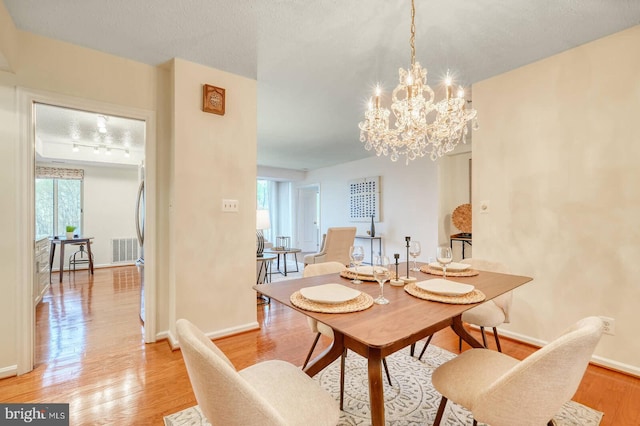 dining room with light wood-style flooring, baseboards, a notable chandelier, and visible vents
