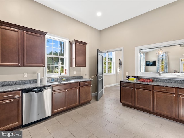 kitchen with a sink, dishwasher, light tile patterned floors, baseboards, and dark stone counters