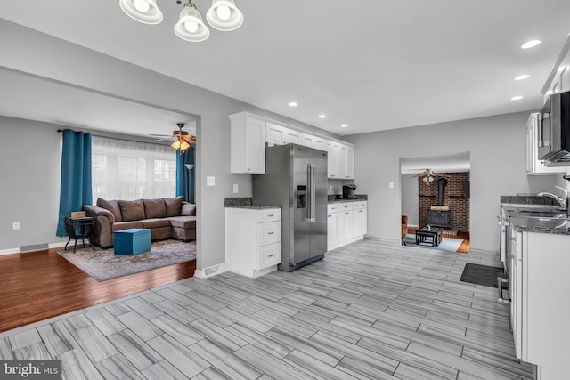 kitchen with open floor plan, a wood stove, stainless steel appliances, white cabinets, and wood tiled floor