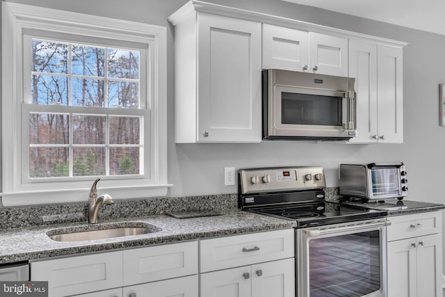 kitchen with white cabinets, a sink, stainless steel appliances, and light stone counters