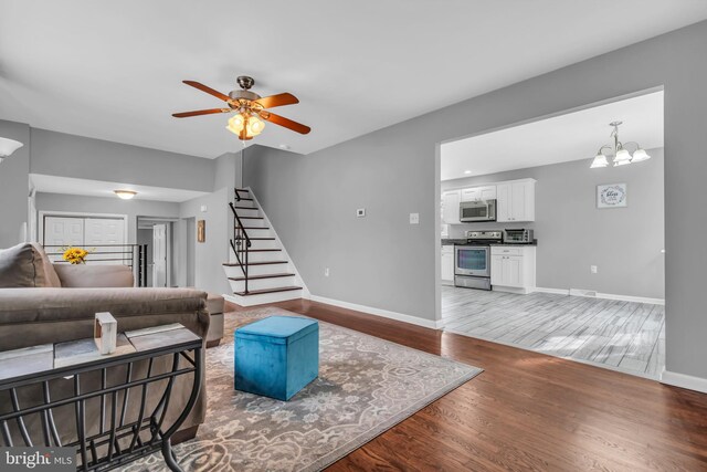 living room featuring stairs, baseboards, ceiling fan with notable chandelier, light wood-style floors, and a toaster