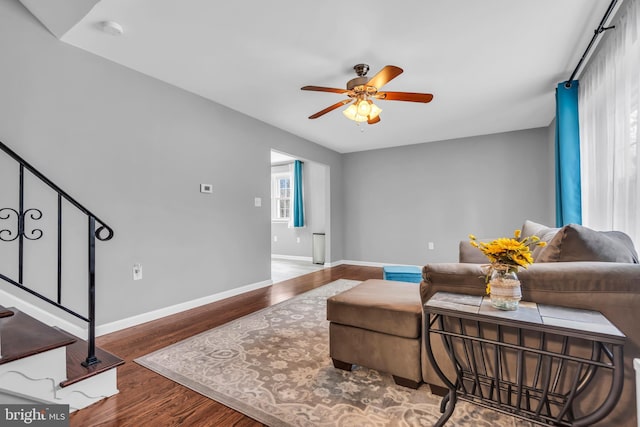 living room featuring baseboards, wood finished floors, stairway, and a ceiling fan