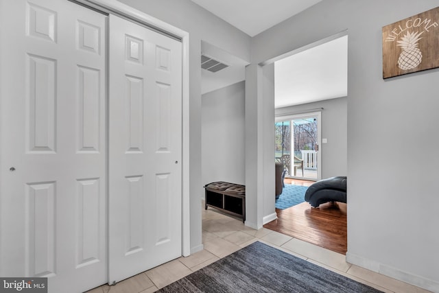 corridor with baseboards, visible vents, and light tile patterned floors