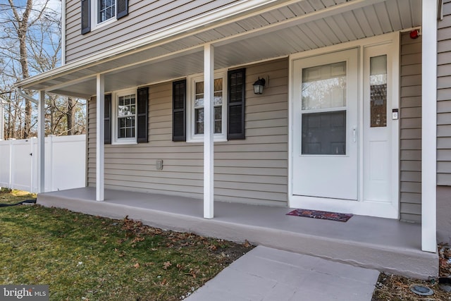 doorway to property with covered porch and fence