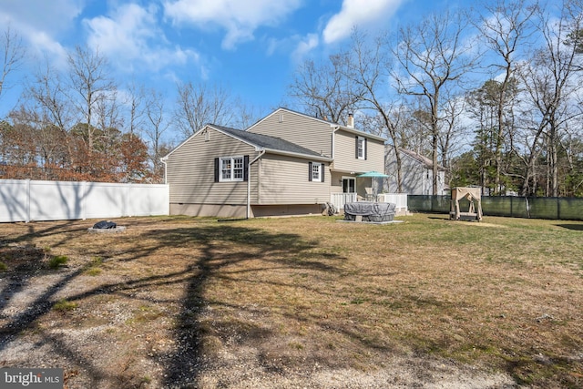 rear view of house featuring a lawn, a chimney, and fence